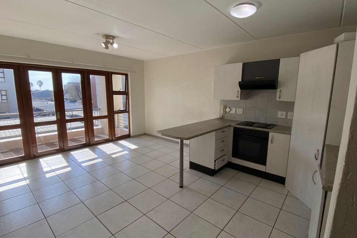 Open-plan living area featuring a functional kitchen with built-in appliances, tiled flooring, and large sliding doors leading to a balcony.