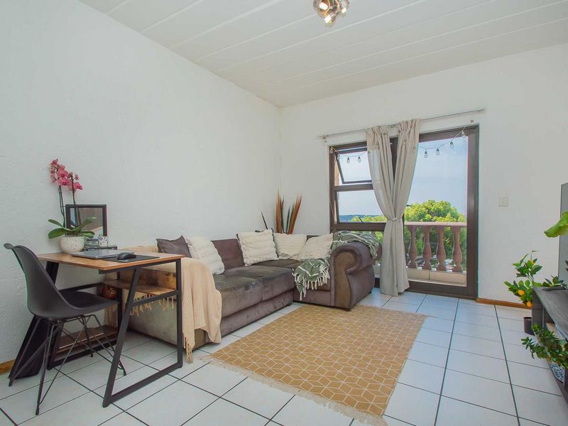 A bright living room featuring white walls, tiled flooring, and a sliding glass door providing direct access to an outdoor balcony area.