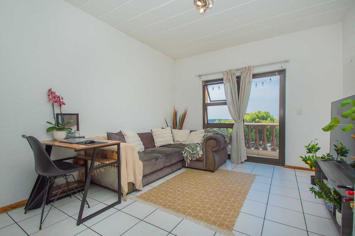 A bright living room featuring white walls, tiled flooring, and a sliding glass door providing direct access to an outdoor balcony area.
