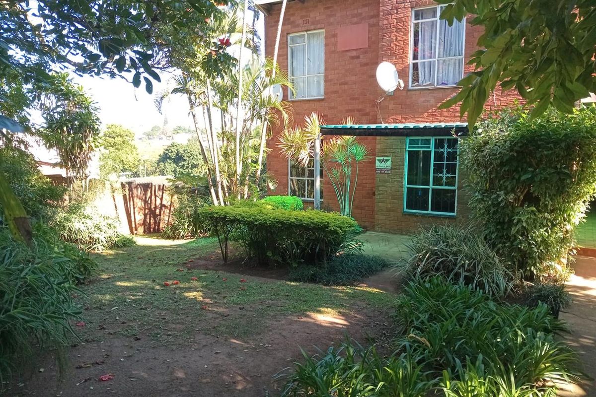 A view of the rear exterior of the apartment building featuring a face brick facade, a small patio area, and a private garden space.