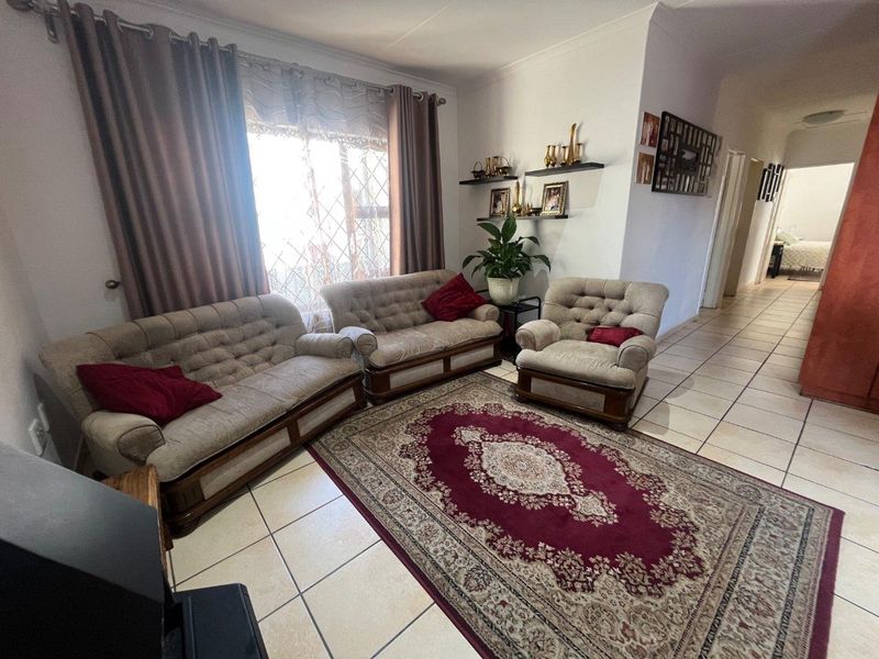 A comfortable living room featuring ceramic floor tiles and a large window with security gate, providing access to the hallway and adjacent bedroom.