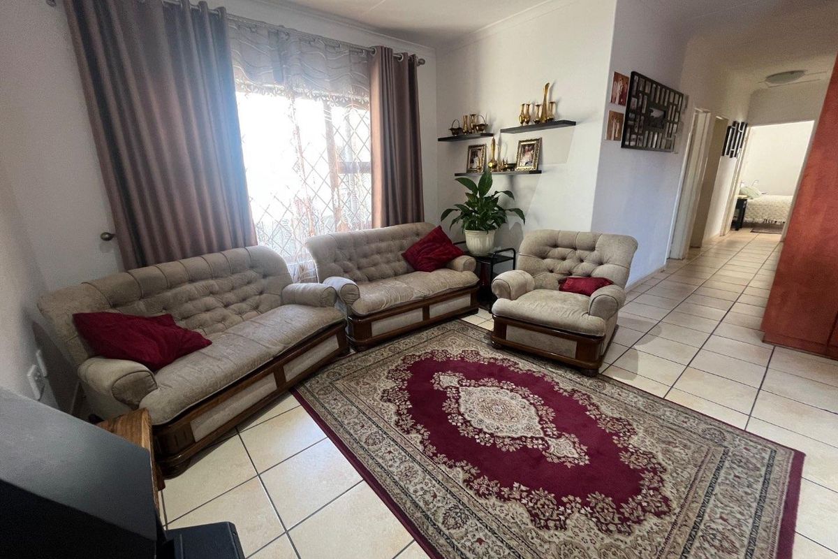 A comfortable living room featuring ceramic floor tiles and a large window with security gate, providing access to the hallway and adjacent bedroom.
