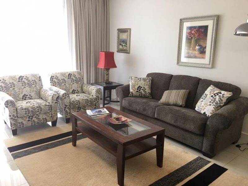 A comfortable living room featuring tiled flooring and full-length curtains, providing a bright and inviting space for relaxation.