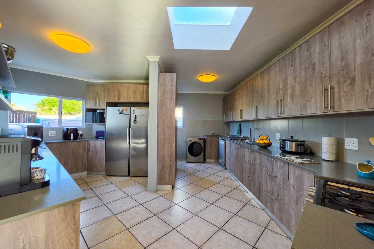 Spacious kitchen featuring extensive wood-finish cabinetry, stone countertops, a large skylight, and integrated appliances, offering a functional and well-lit culinary workspace.