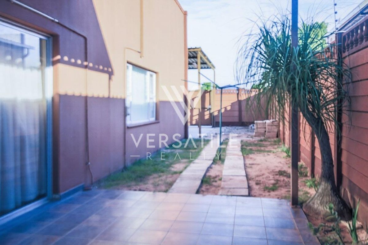 A rear exterior view of the property featuring a tiled patio area, paved walkway, and perimeter walling with security fencing.
