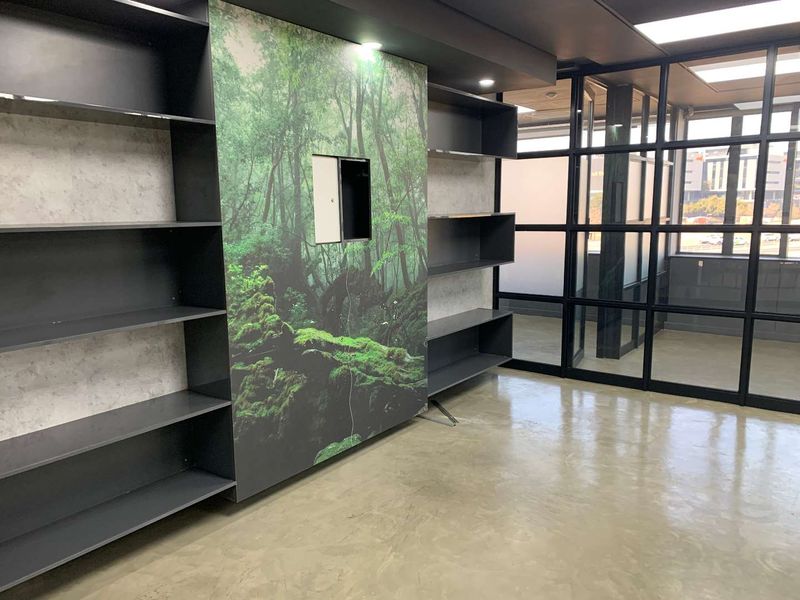 Modern office space featuring built-in shelving, polished concrete floors, and a sleek black-framed glass partition wall with natural light.