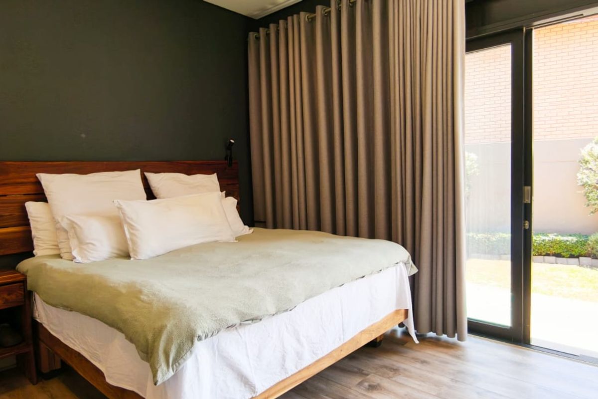 A modern bedroom featuring laminate flooring, a custom wooden headboard, and large sliding glass doors providing direct access to the rear garden.