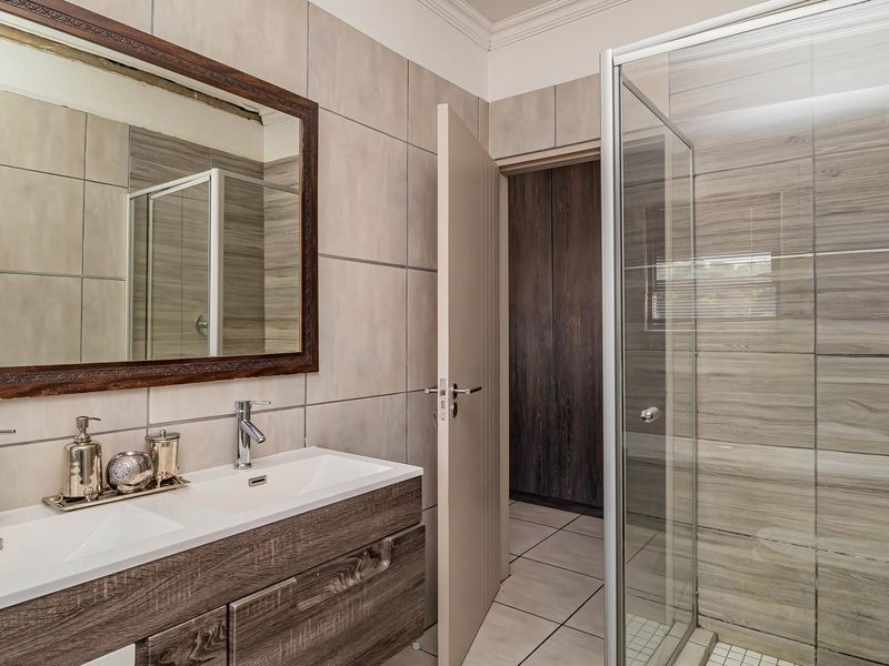 Modern bathroom featuring a double vanity with wood-finish cabinetry, a glass-enclosed shower, and neutral wall tiling.