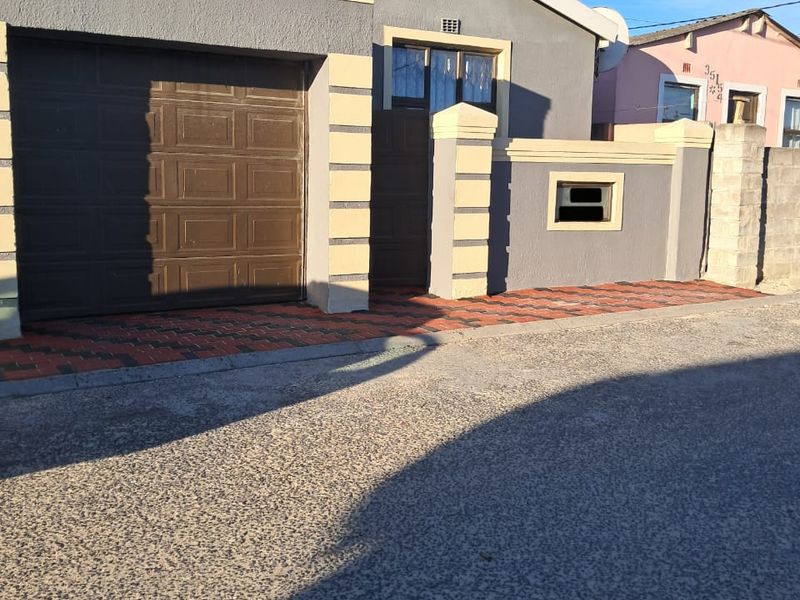 Front elevation of a residential property featuring a single garage, paved driveway, and a secure boundary wall.