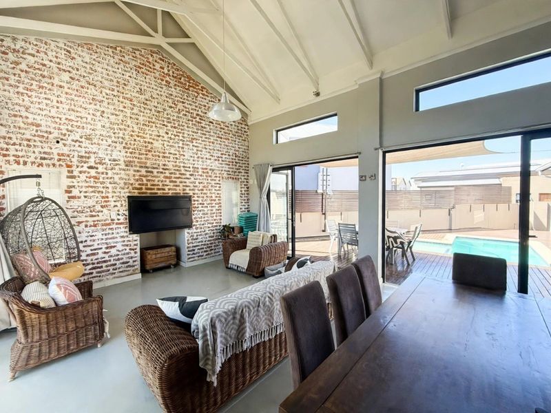 Spacious open-plan living area featuring a striking exposed brick wall, vaulted ceilings, and large sliding doors that open onto a private pool deck.