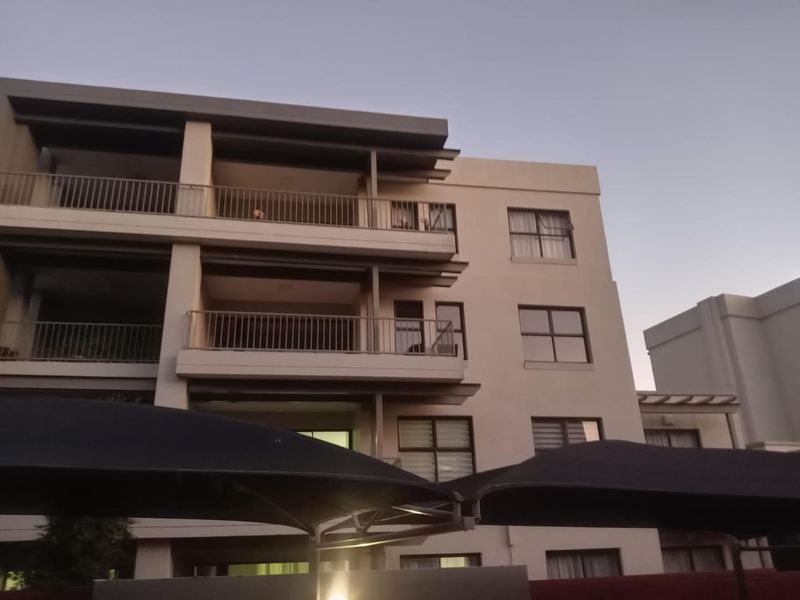 Exterior view of a modern apartment building featuring multiple levels with private balconies, metal railings, and large aluminium-framed windows.