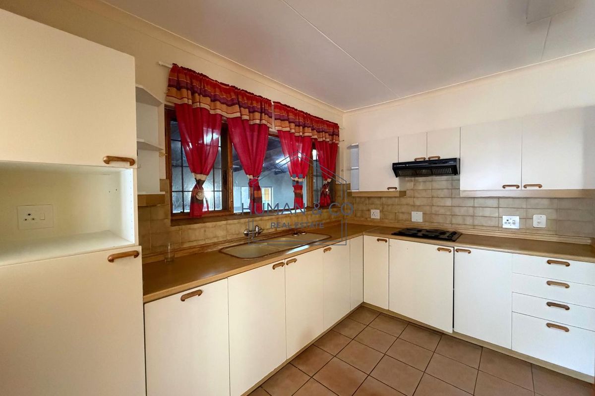 A functional kitchen featuring white cabinetry, laminate countertops, a built-in hob with extractor fan, and tiled flooring.