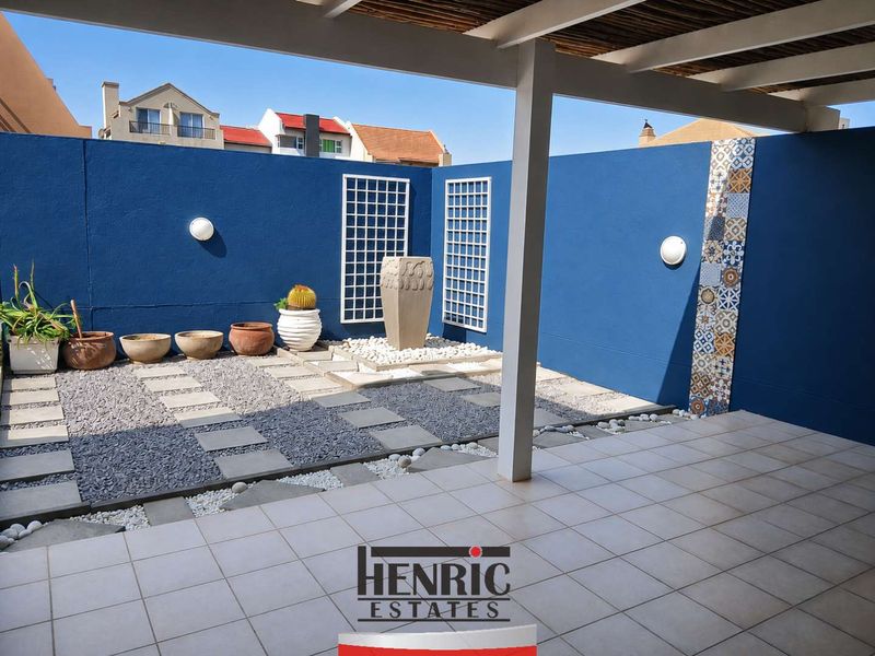 A well-maintained covered patio featuring tiled flooring, decorative wall accents, and a landscaped stone garden area.
