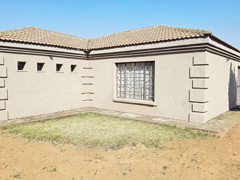 Rear view of a single-story house featuring a tiled roof, textured plaster walls, and security bars on the windows.