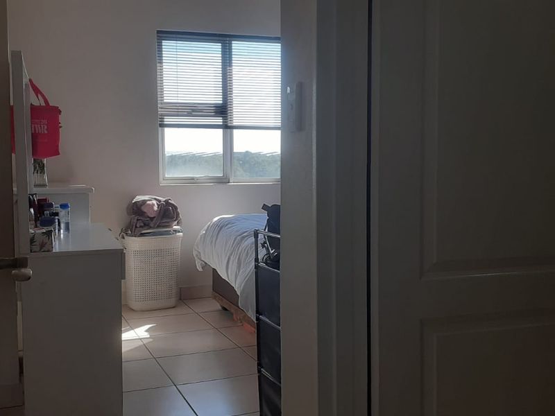A view into a bedroom featuring tiled flooring and a window with venetian blinds, viewed from an adjacent hallway.