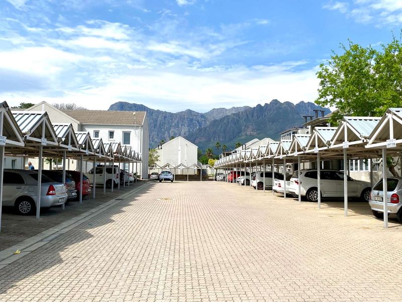 A well-maintained apartment complex parking area featuring numerous covered parking bays with paved surfaces and scenic mountain views in the background.