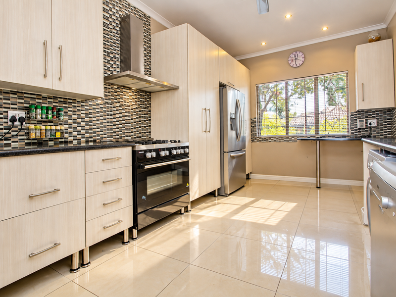 Modern kitchen featuring light wood-grain cabinetry, mosaic tile backsplash, stainless steel appliances, and polished porcelain floor tiles with a convenient breakfast bar area.