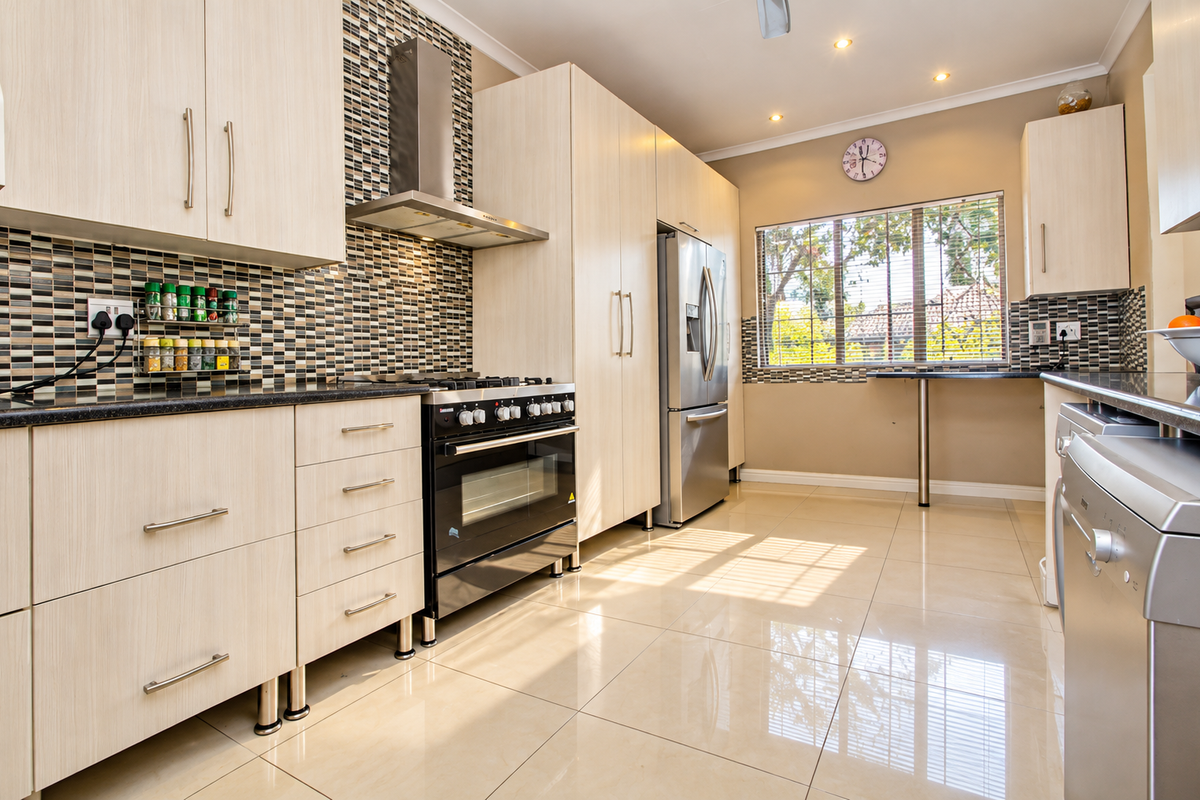 Modern kitchen featuring light wood-grain cabinetry, mosaic tile backsplash, stainless steel appliances, and polished porcelain floor tiles with a convenient breakfast bar area.