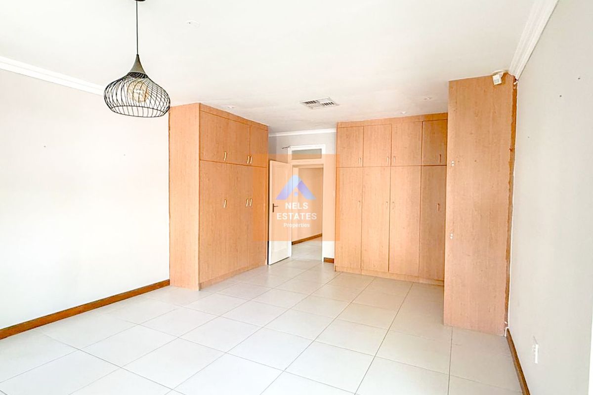 A spacious bedroom featuring extensive built-in wooden cabinetry, neutral floor tiling, and a modern pendant light fixture.