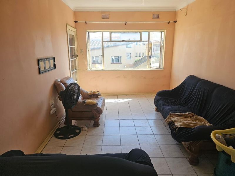 A living room featuring tiled flooring, large windows, and wall-mounted ventilation grilles, currently requiring cosmetic updates to the wall finishes.