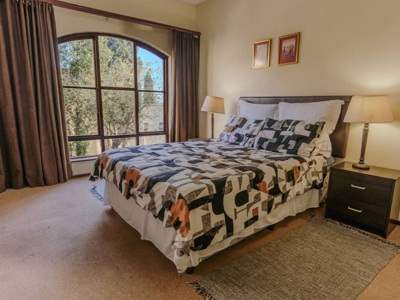 A comfortable bedroom featuring a large arched window that provides natural light and views of the surrounding trees.