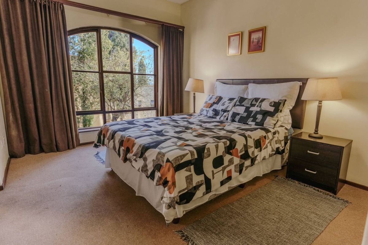 A comfortable bedroom featuring a large arched window that provides natural light and views of the surrounding trees.
