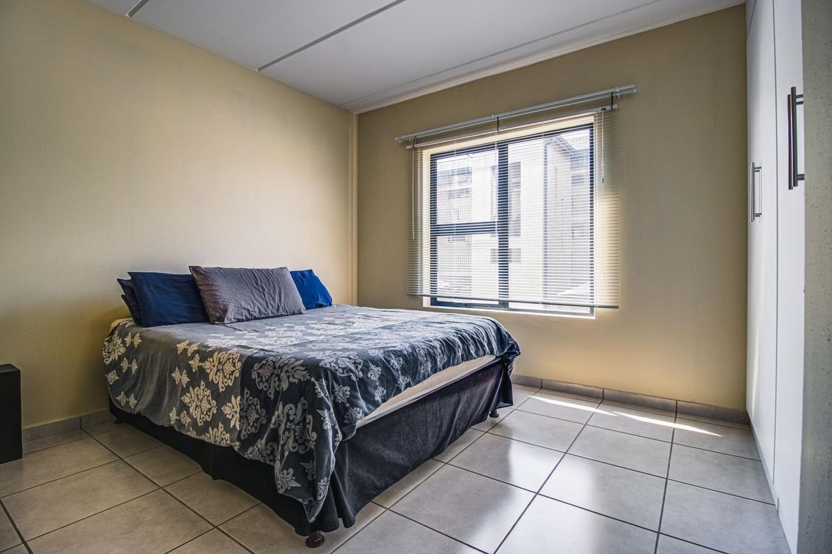 A functional bedroom featuring neutral wall tones, tiled flooring, a built-in wardrobe, and a window with fitted blinds.