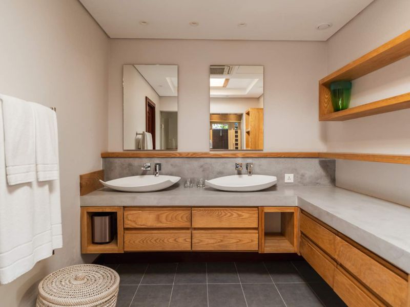 Modern bathroom featuring a double vanity with concrete countertop, integrated wooden cabinetry, dual vessel sinks, and wall-mounted mirrors.