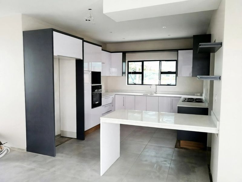 Modern, newly installed kitchen featuring high-gloss cabinetry, stone countertops, a central island, and integrated oven and hob.