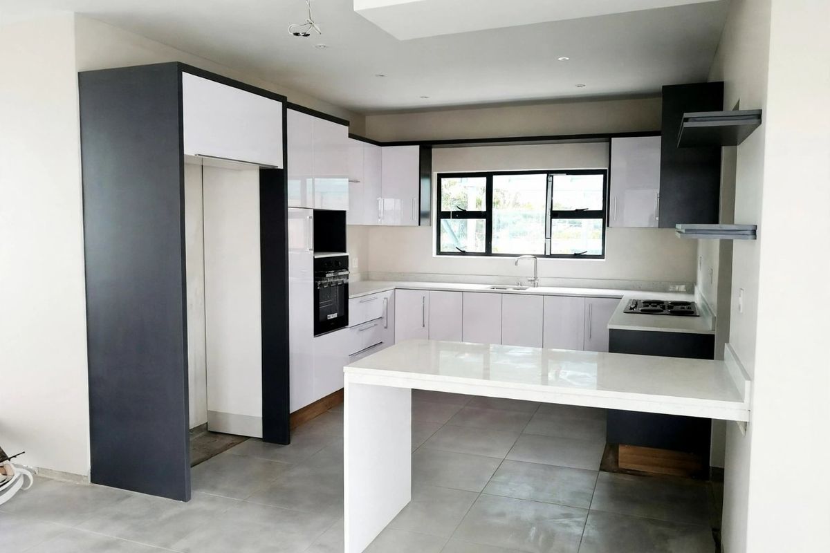 Modern, newly installed kitchen featuring high-gloss cabinetry, stone countertops, a central island, and integrated oven and hob.