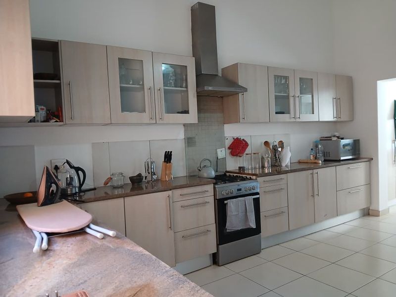 A functional kitchen featuring light wood-finish cabinetry, granite countertops, a stainless steel extractor fan, and a freestanding oven with a tiled splashback.