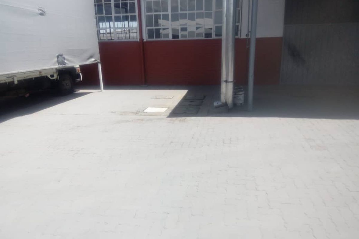 Exterior view of an industrial loading area featuring paved ground, metal industrial ducting, and large multi-pane windows on the building facade.