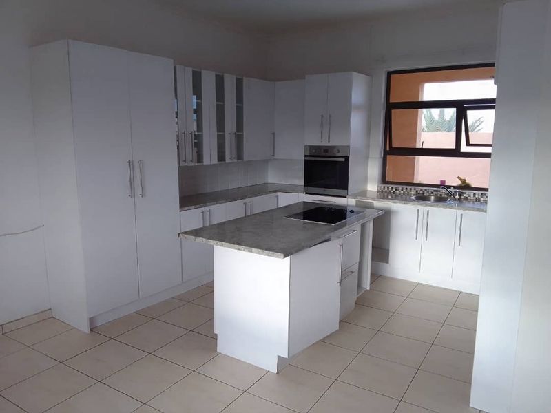Modern kitchen featuring white cabinetry, a central island with a built-in hob, stone countertops, and tiled flooring.