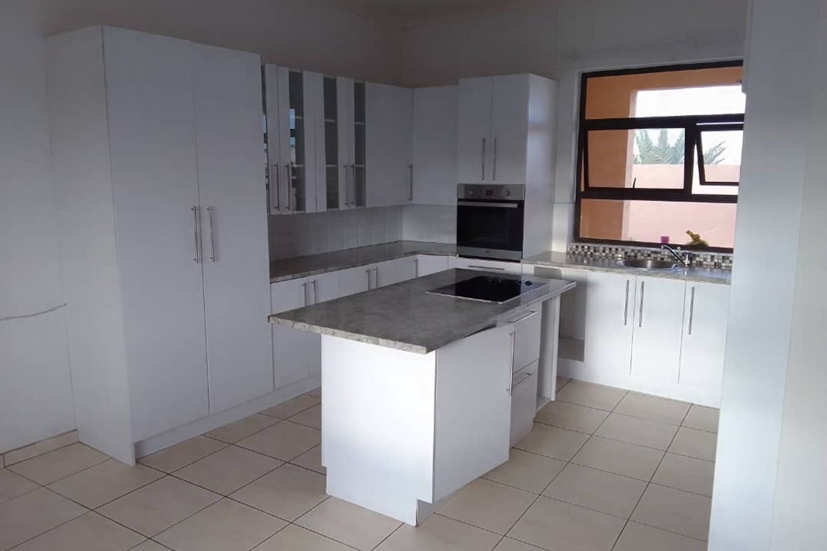 Modern kitchen featuring white cabinetry, a central island with a built-in hob, stone countertops, and tiled flooring.