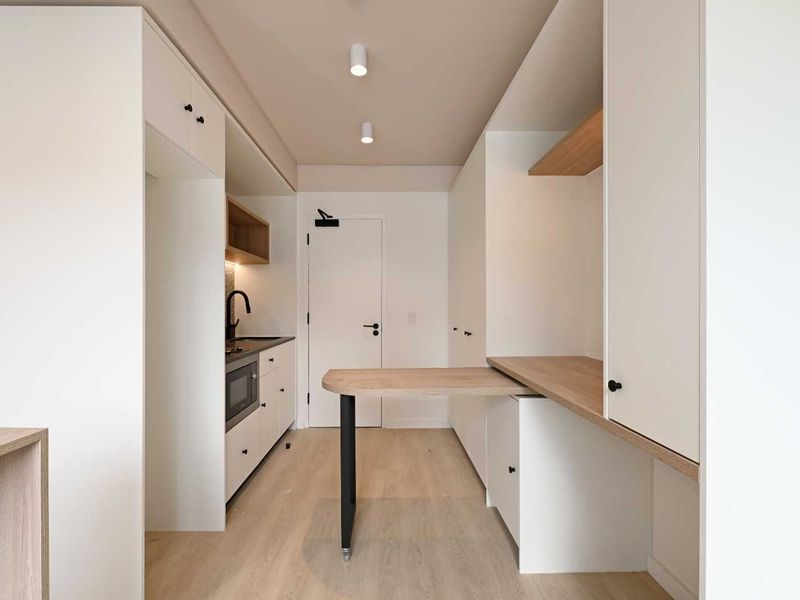 Modern, minimalist kitchen featuring sleek white cabinetry, integrated appliances, light wood-tone finishes, and a functional built-in desk area.