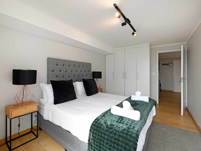 A well-maintained bedroom featuring built-in cupboards, modern track lighting, and light-toned laminate flooring, offering a clean and functional living space.