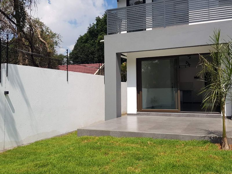 Rear view of the cottage featuring a tiled patio, sliding door access, and a private garden area with perimeter wall and electric fencing.