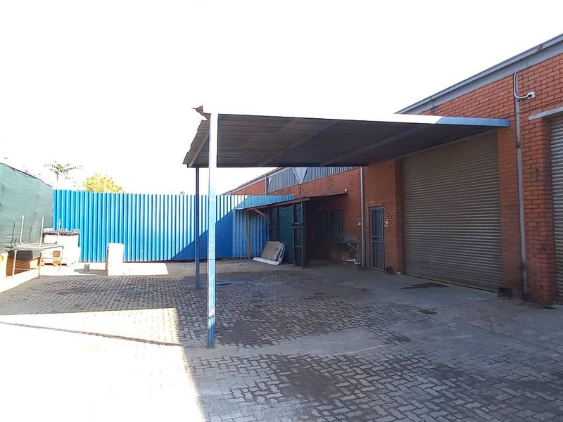 Industrial yard area featuring paved ground, a covered loading bay, and secure roller shutter doors for efficient access.