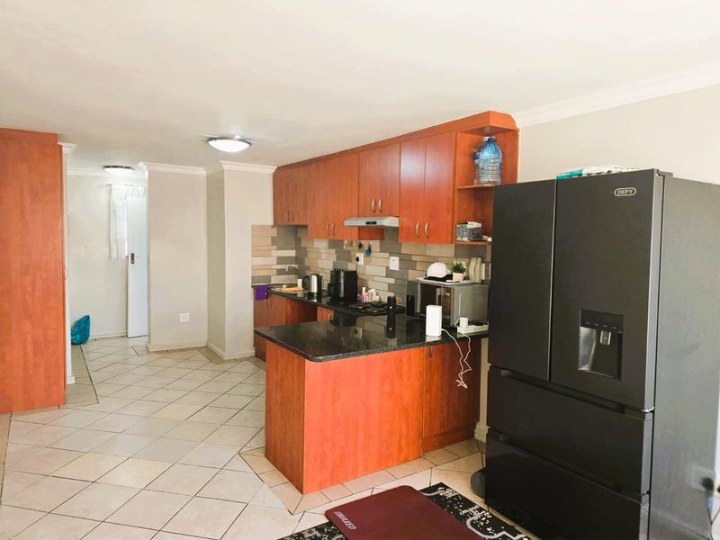 A functional kitchen featuring warm-toned laminate cabinetry, granite countertops, a tiled backsplash, and integrated cooking appliances with ceramic floor tiles.