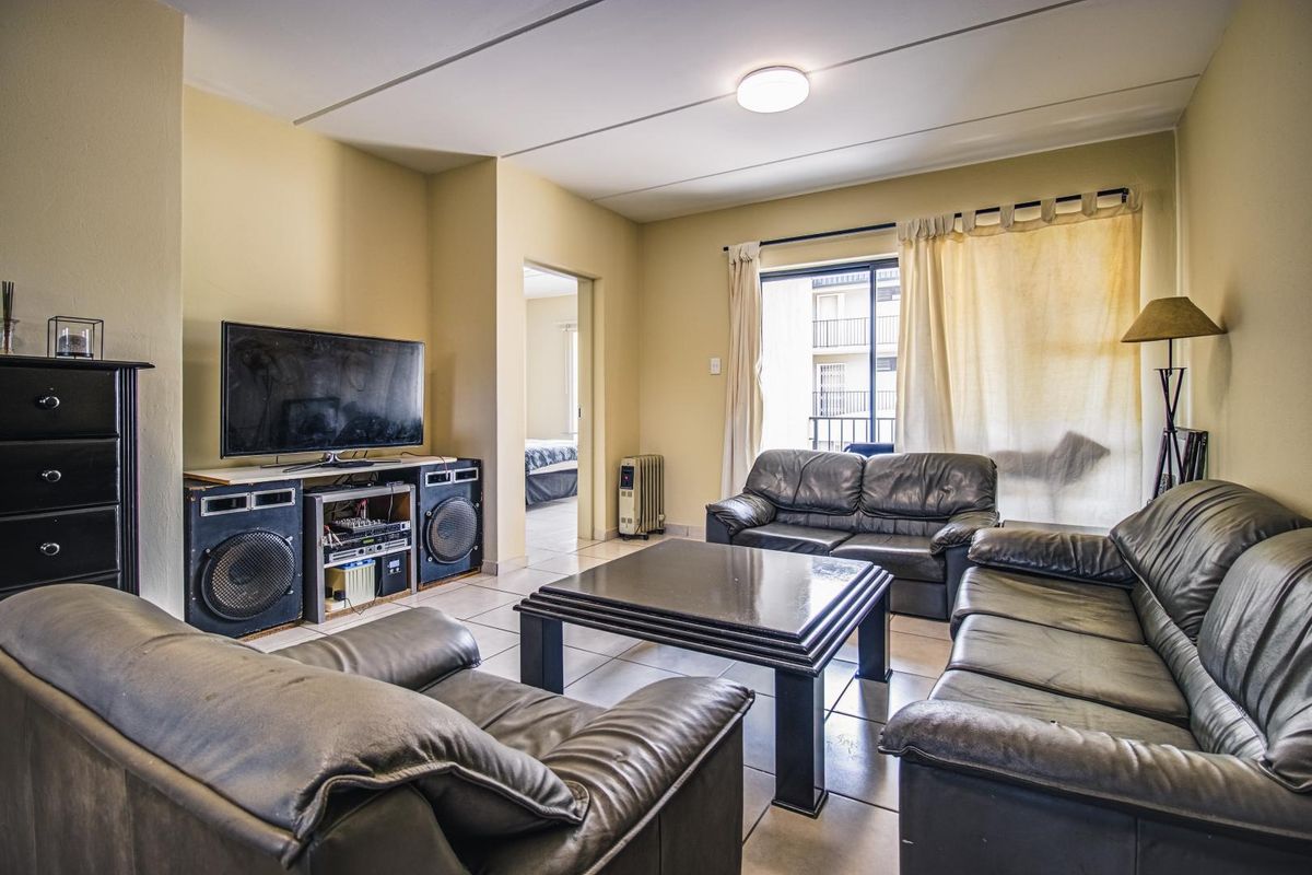 A living room featuring tiled flooring, a sliding door leading to a balcony, and a doorway providing access to an adjacent bedroom.