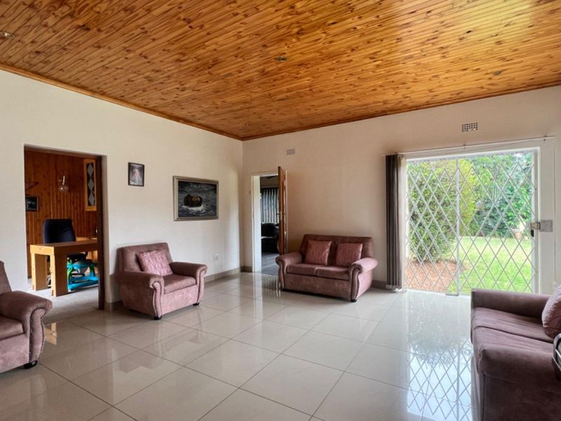Spacious living room featuring a warm timber tongue and groove ceiling, polished porcelain floor tiles, and direct access to the garden via a sliding door.