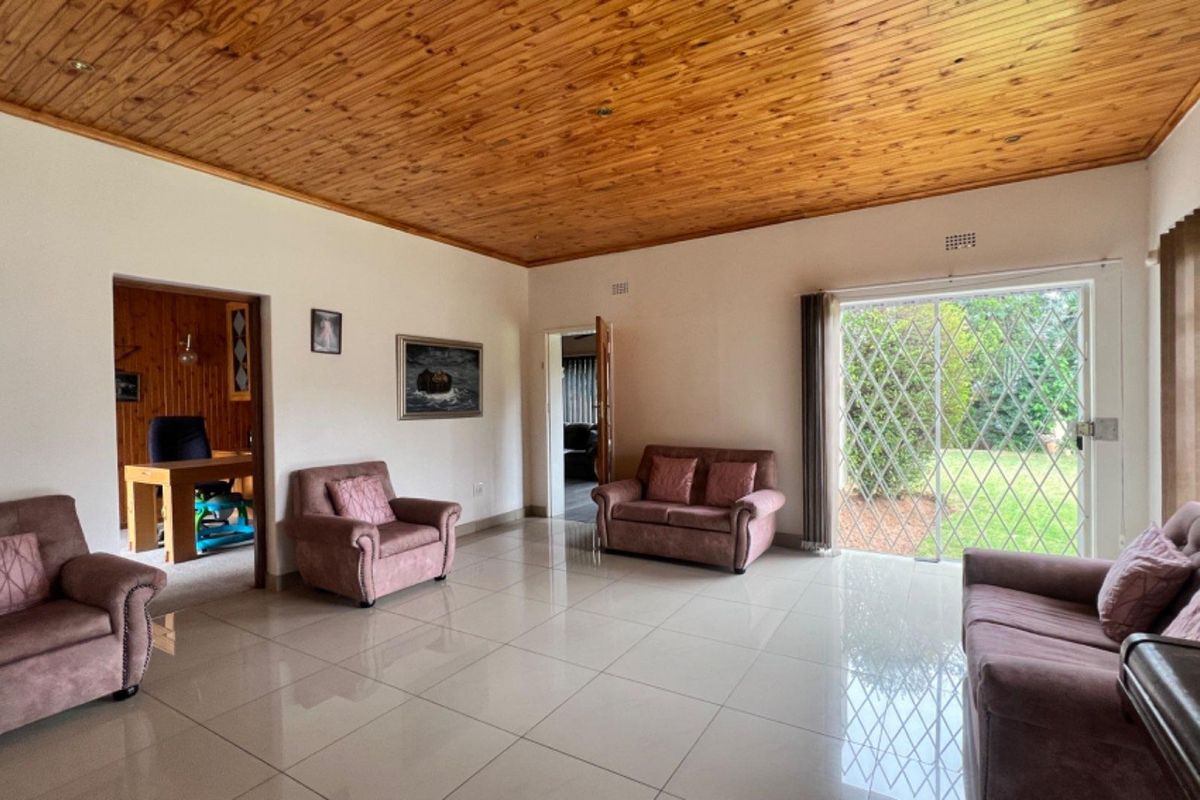 Spacious living room featuring a warm timber tongue and groove ceiling, polished porcelain floor tiles, and direct access to the garden via a sliding door.