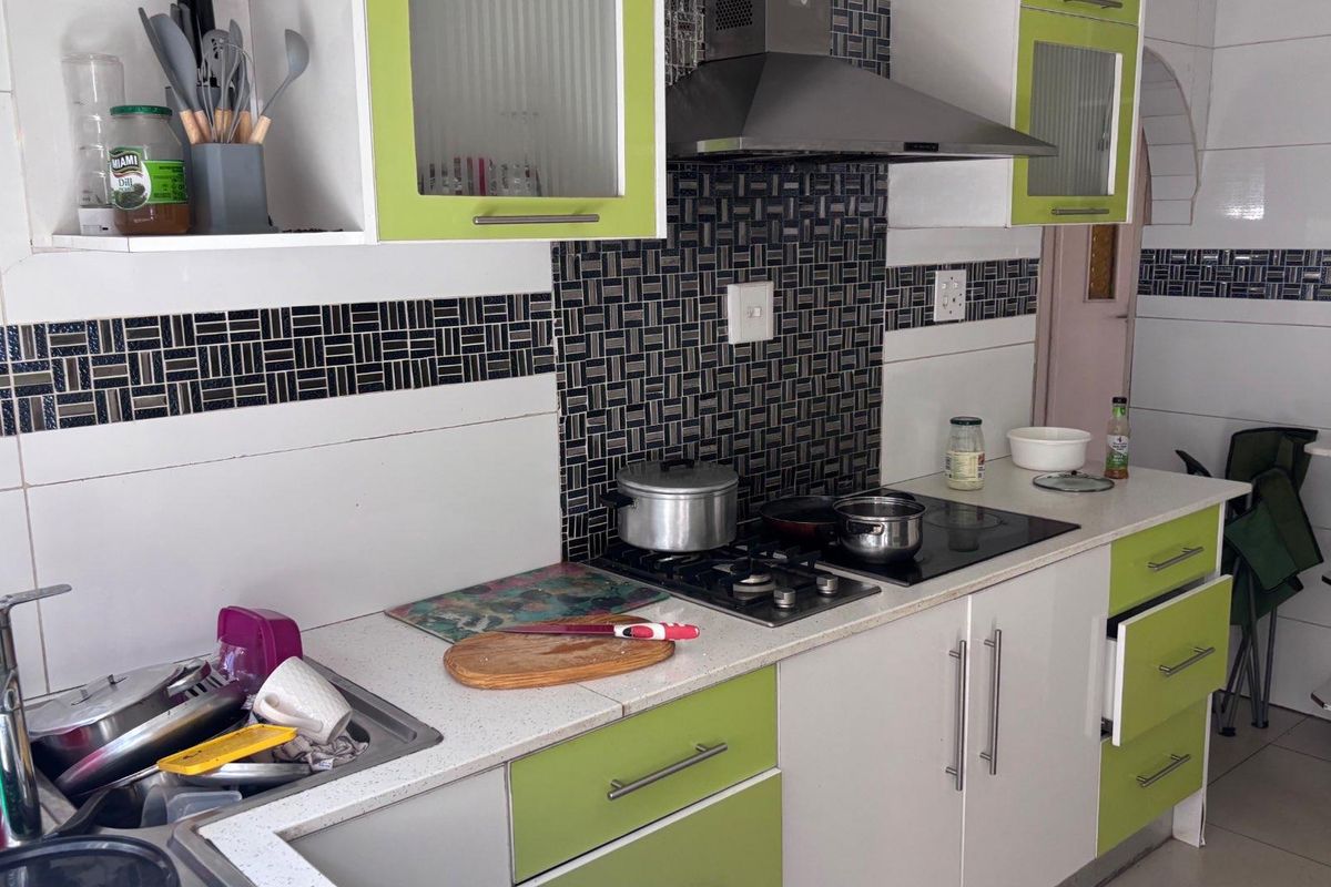 A functional kitchen featuring lime green and white cabinetry, a mosaic tile backsplash, a gas hob with an extractor fan, and a stainless steel sink.