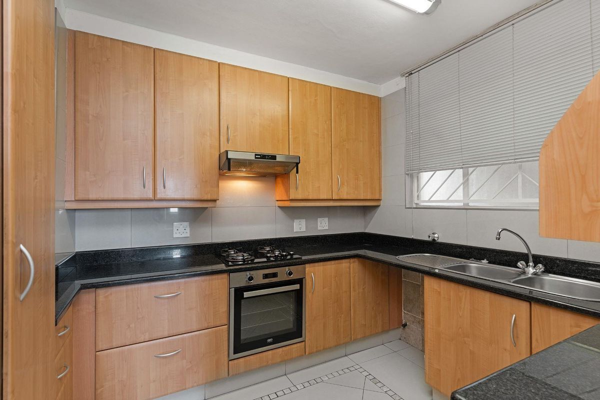 A functional kitchen featuring light wood cabinetry, granite countertops, a gas hob, built-in oven, and tiled finishes throughout.