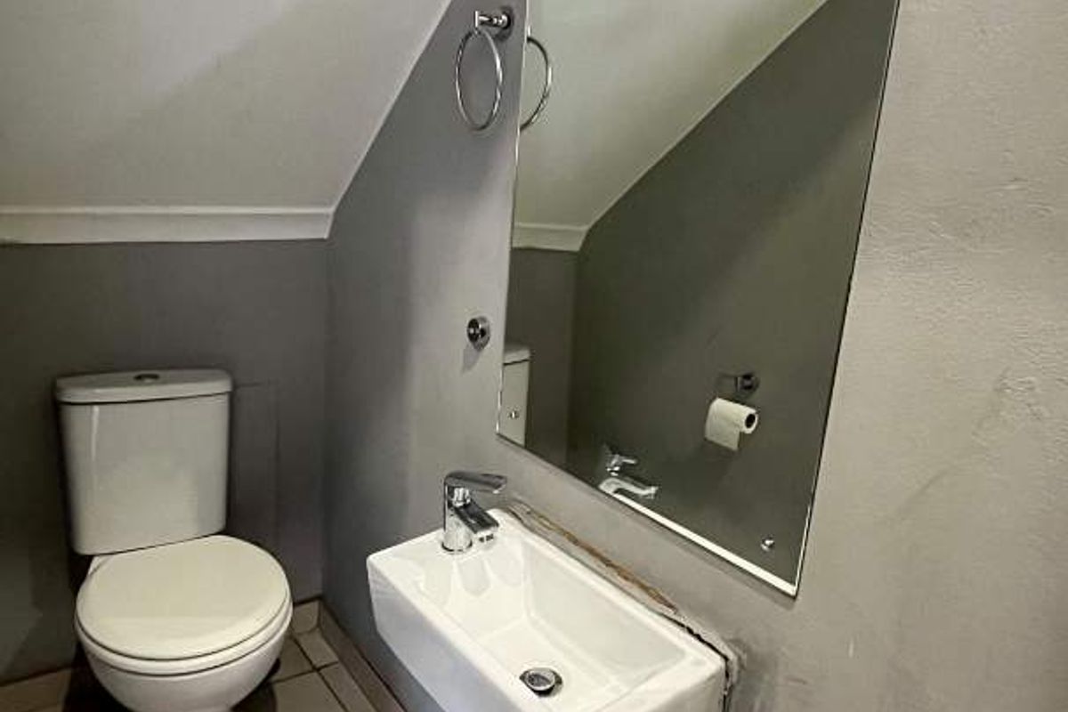 A compact guest bathroom featuring a wall-mounted basin, toilet, and mirror, situated under a sloped ceiling.