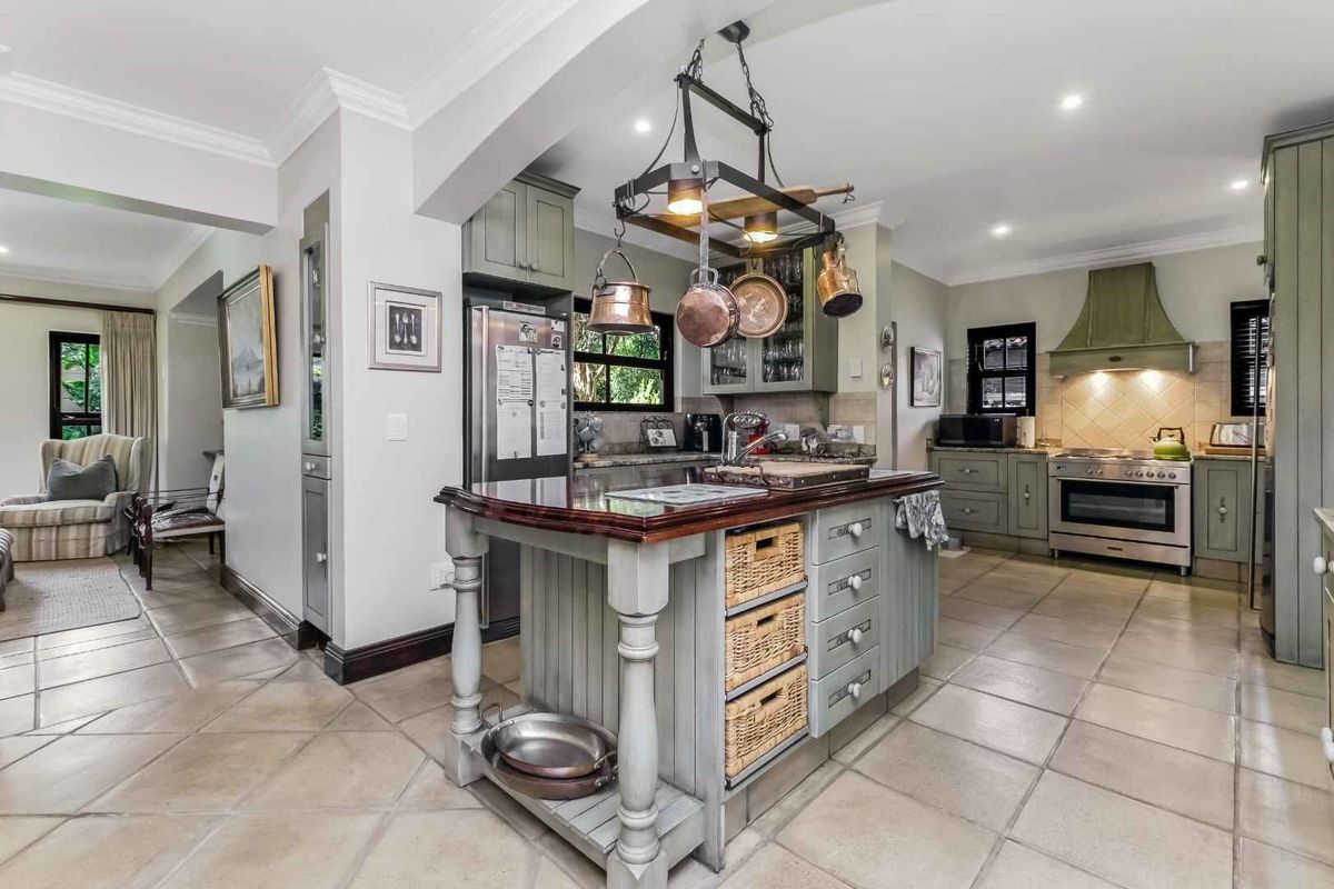 A well-appointed kitchen featuring a central island with a wooden countertop, custom cabinetry, a gas range with a decorative hood, and tiled flooring.