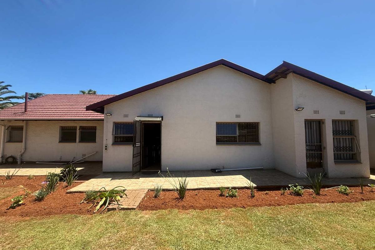 Rear view of the house featuring a tiled patio area, security gates on entrances, and security bars on windows, set against a landscaped garden.
