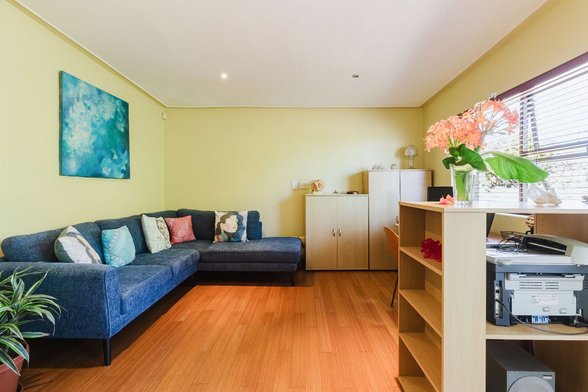 A comfortable living room featuring warm-toned laminate flooring, recessed ceiling lighting, and large windows fitted with venetian blinds.