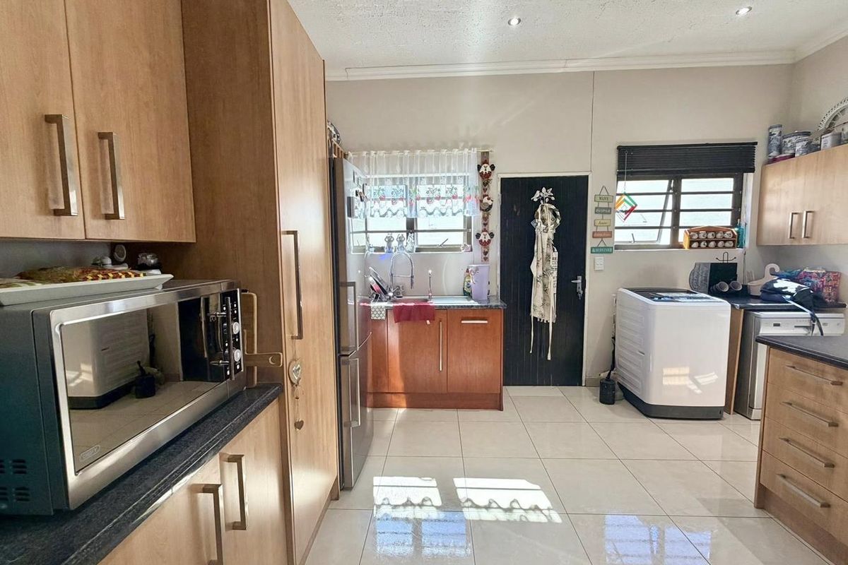 Functional kitchen featuring light wood-toned cabinetry, dark countertops, tiled flooring, and integrated laundry plumbing connections.