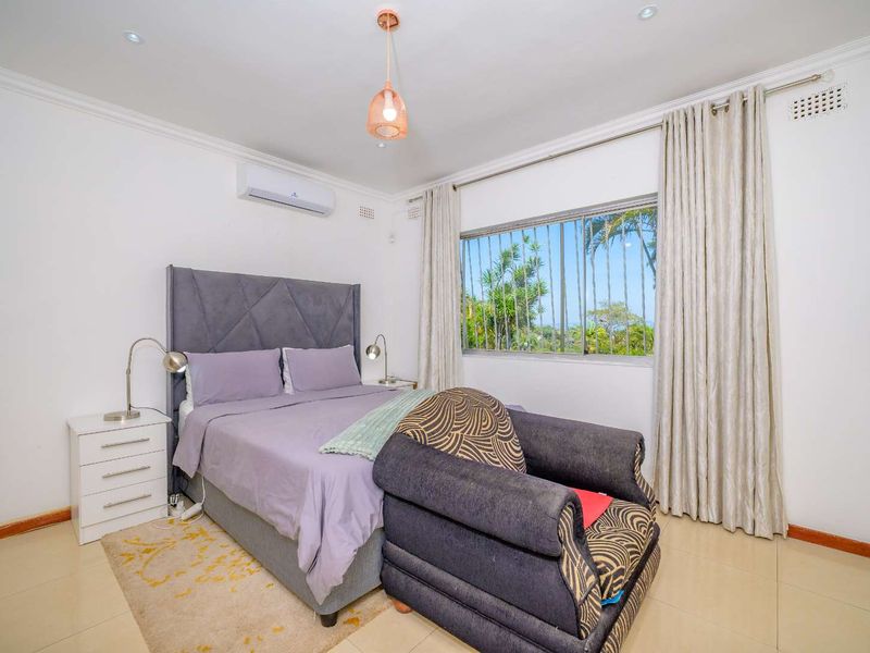 A well-maintained bedroom featuring tiled flooring, an air conditioning unit, recessed lighting, and built-in cupboards with security bars on the window.